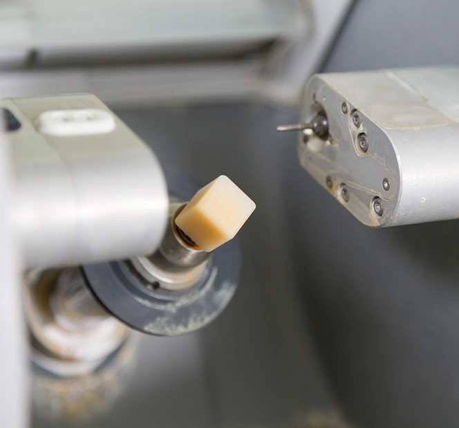 Close-up of a dental milling machine holding a ceramic block, preparing a tooth restoration.